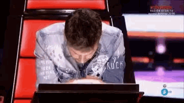 a man in a denim jacket is sitting in a chair with his head down .