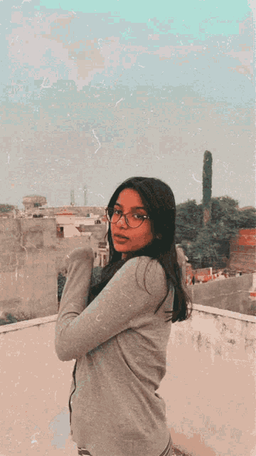 a young woman wearing glasses and a grey sweater poses for a picture