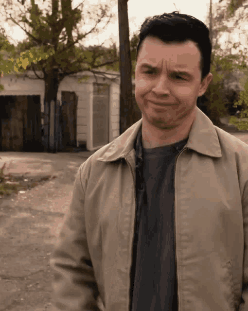 a man wearing a tan jacket and a black shirt is making a funny face