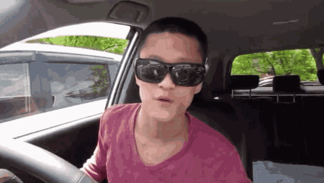 a man wearing sunglasses is driving a car .