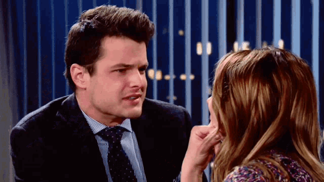 a man and woman are looking at each other and the woman is touching the man 's face