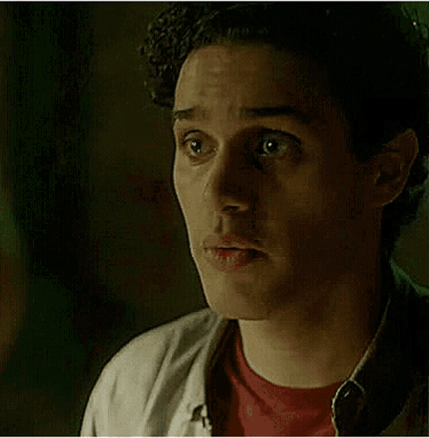 a young man with curly hair is wearing a red shirt and a white shirt and making a funny face .