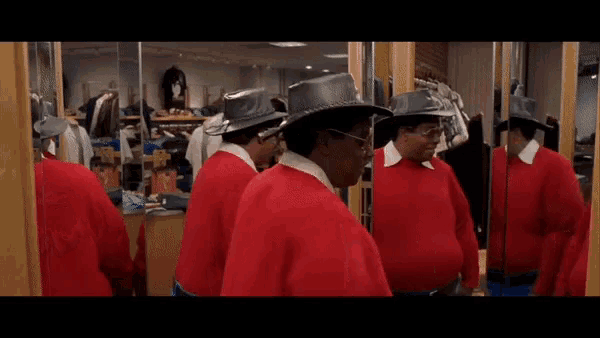 a man in a red sweater is looking at his reflection in the mirror