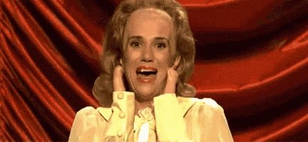 a woman in a yellow dress is making a funny face while standing in front of a red curtain .