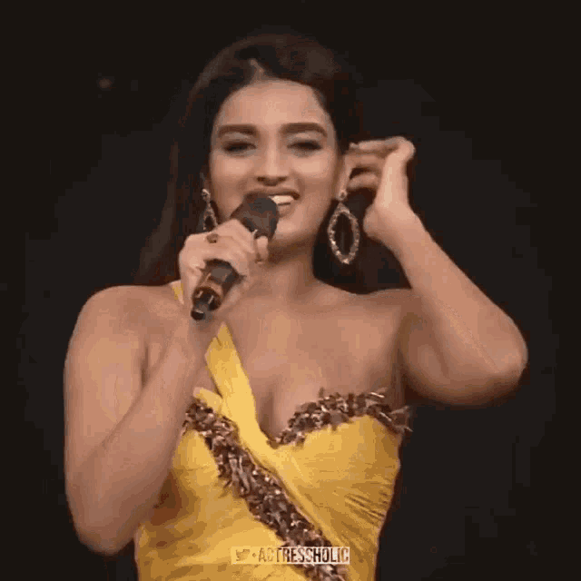 a woman in a yellow dress is holding a microphone in her hand .