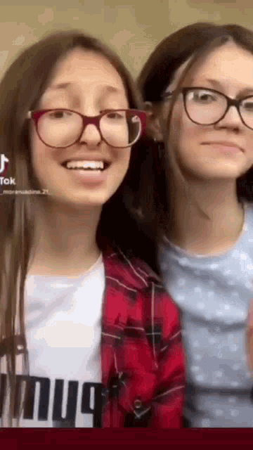 two girls wearing glasses are standing next to each other and smiling for the camera .