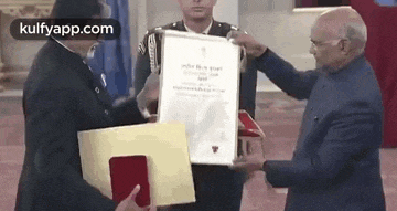 a man is giving a certificate to another man while a man in a military uniform stands behind them .