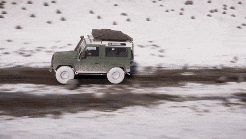 a green jeep is driving through the snow