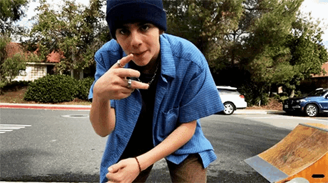 a young man wearing a blue shirt and a black beanie is standing on a street