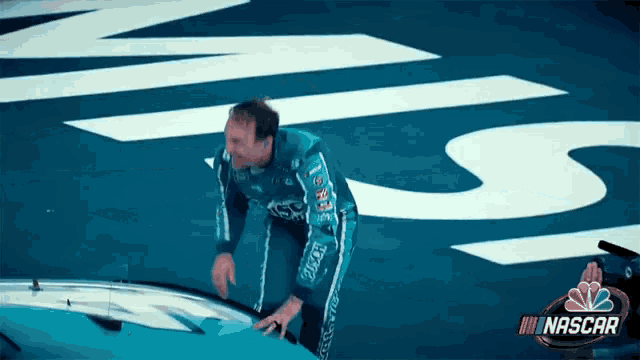 a man in a nascar uniform stands next to a blue car