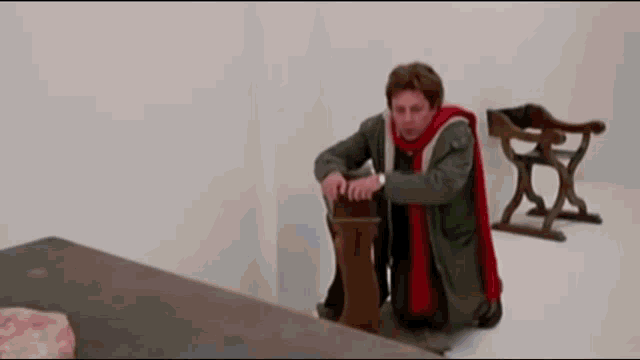 a man in a green coat and red scarf is kneeling down next to a wooden table .