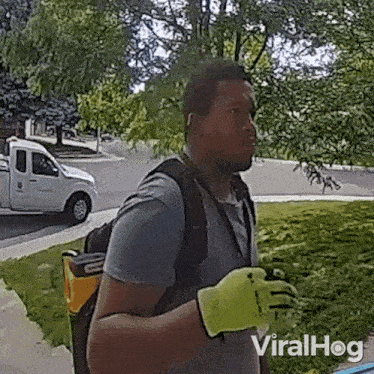 a man wearing yellow gloves and a backpack is standing in front of a truck .