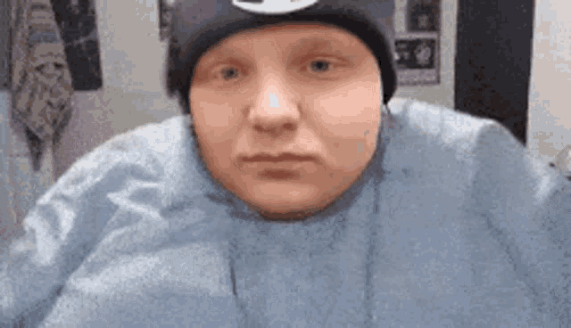 a man wearing a beanie and a blue sweater is making a funny face .