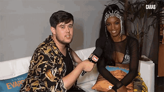 a man and a woman are sitting on a couch with a microphone in their hands .