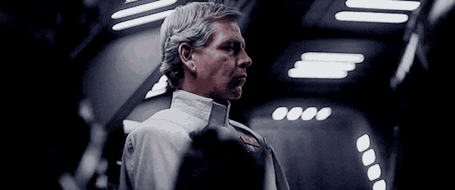 a man in a white uniform is standing in a dark room with lights behind him