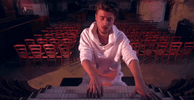 a man in a white hoodie is playing a piano