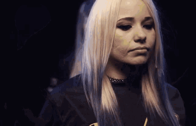 a woman with blonde hair is wearing a choker and a black shirt with the letter a on it