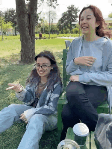 two girls are sitting on a bench in a park laughing and talking .
