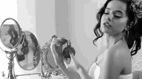 a woman is applying perfume in front of a mirror .