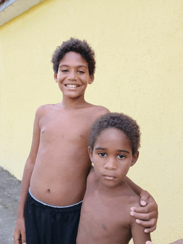 two young boys standing next to each other in front of a yellow wall and smiling