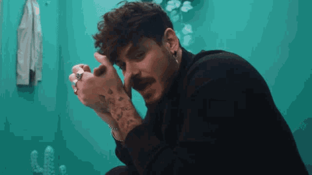 a man with a mustache is sitting in front of a blue wall
