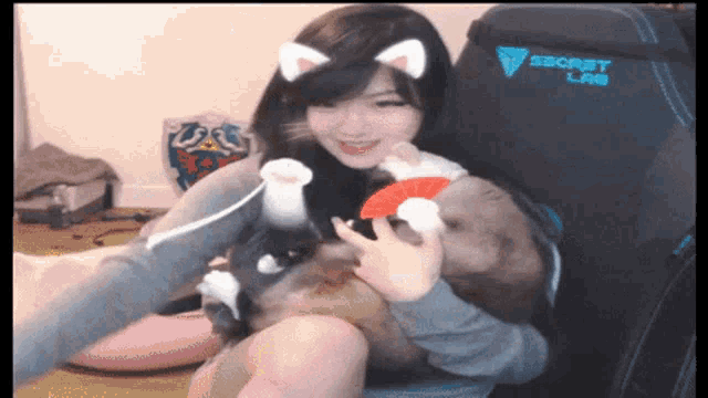 a woman is holding a cat in front of a secret lab gaming chair
