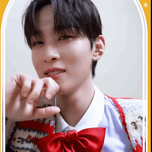 a young man wearing a red bow tie and a sweater is making a heart with his hands .