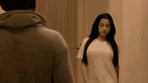 a woman in a white shirt is standing in front of a man in a grey hoodie