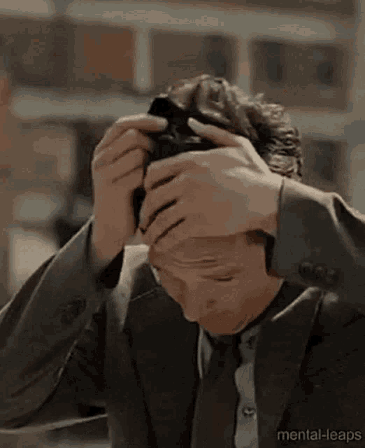 a man in a suit and tie is holding his head in pain .