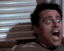 a man with his mouth open is sitting in front of a window .