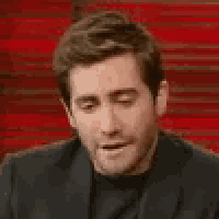 a man in a suit is making a funny face while sitting in front of a red wall .