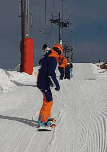 a person on a snowboard going down a snowy slope with a ski lift in the background