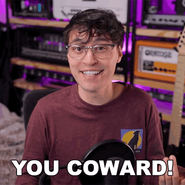 a man with glasses and a shirt that says you coward