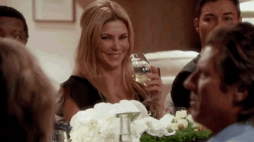 a woman is sitting at a table holding a glass of wine and smiling .