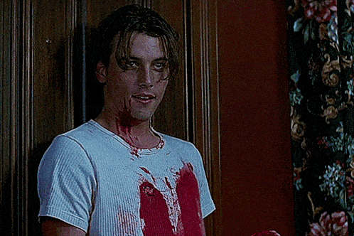 a man with blood on his shirt is standing in front of a door
