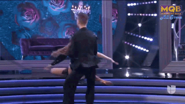 a man is holding a woman in his arms on a stage with mqb written on the bottom right