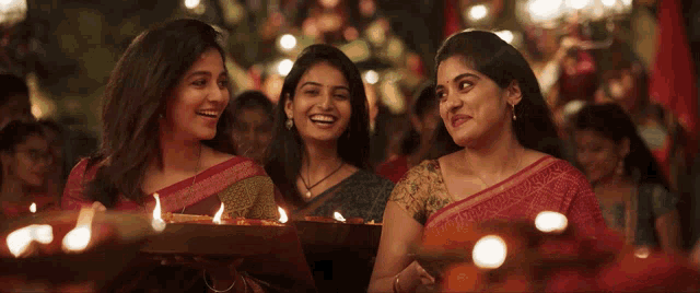 three women are smiling and holding lit candles