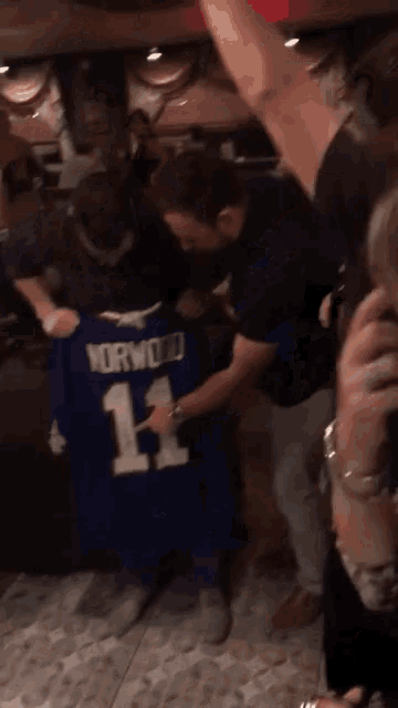 a man holds up a jersey that says horwood 11 on it