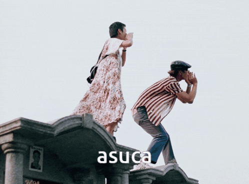 a man and a woman standing on top of a building with the word asuca written below them