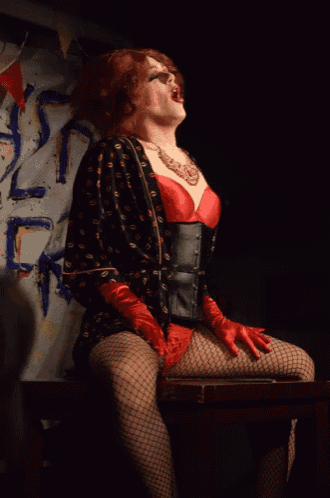 a woman in a red bra and red gloves is sitting on a chair in front of a sign that says t