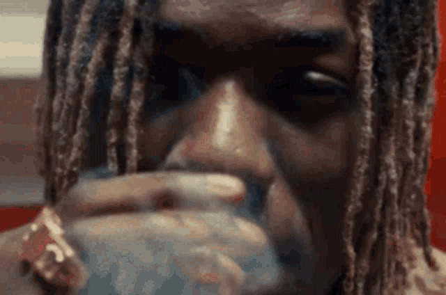 a close up of a man with dreadlocks drinking from a glass