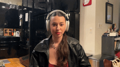 a woman wearing headphones sits at a table in front of a black refrigerator