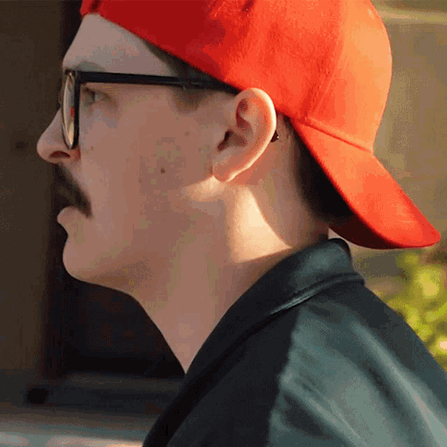 a man wearing glasses and a red hat looks to the side