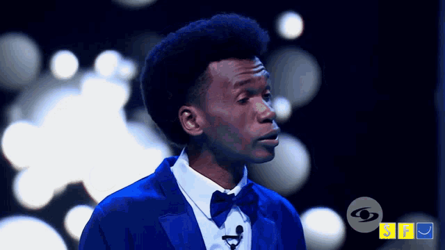 a man in a blue suit and bow tie stands in front of a sign that says sbs