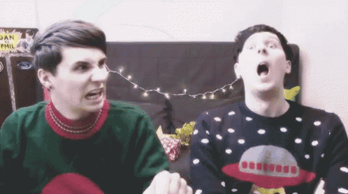 two men wearing ugly christmas sweaters are sitting next to each other on a couch .
