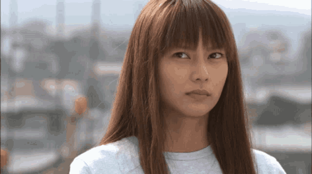 a woman with long hair and bangs is wearing a gray shirt