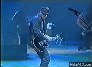 a man is playing a guitar and singing into a microphone while another man stands behind him