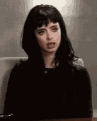 a woman with black hair is sitting at a desk with her mouth open .