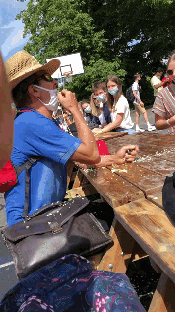 a man wearing a straw hat and sunglasses is sitting at a picnic table with other people