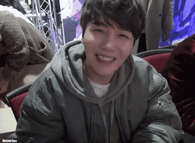 a young man wearing a green jacket and a hoodie smiles